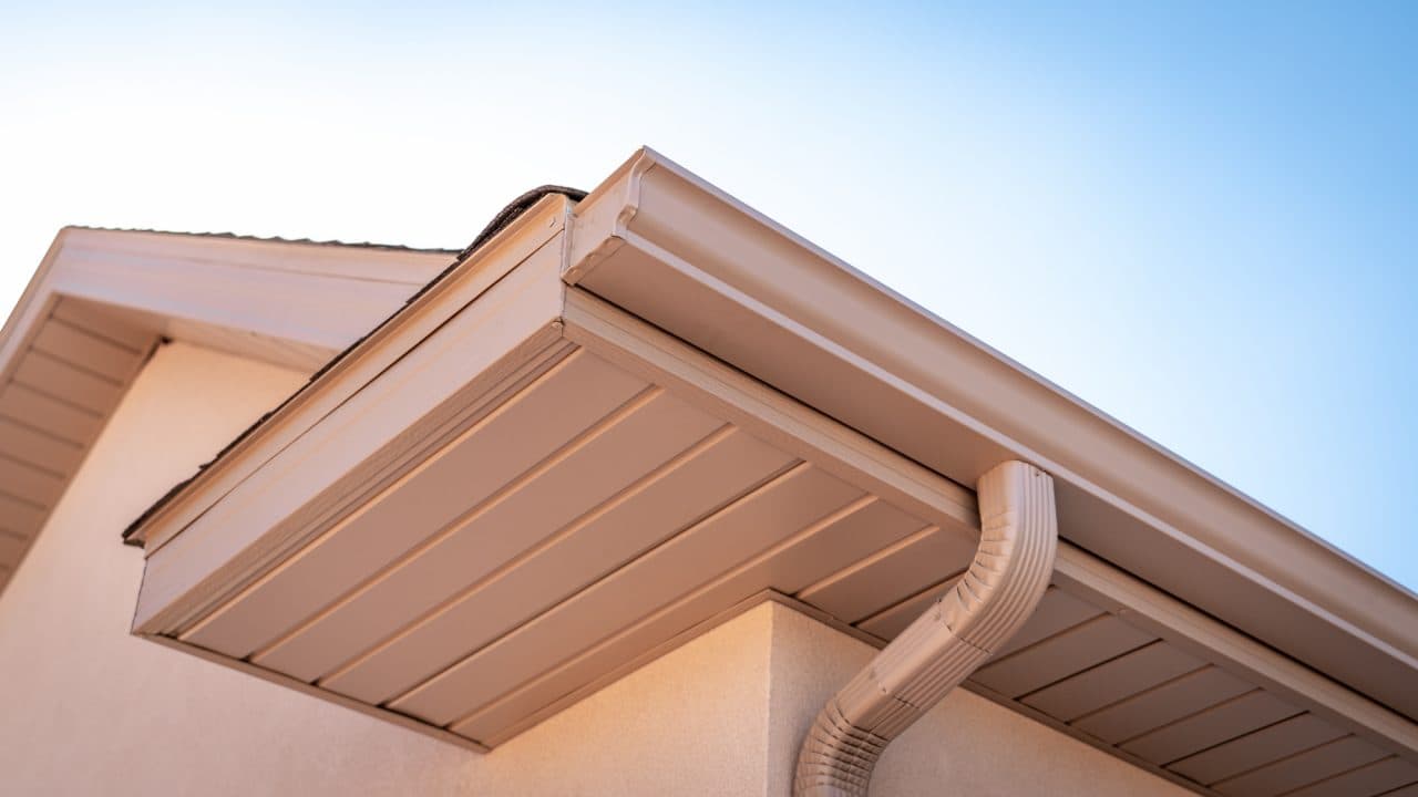Finished white gutter, soffit, fascia and downspout along a stucco roof edge